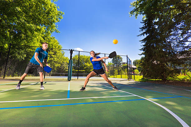 Young Man and Woman Pickleball Player Playing Pickleball in Court A Caucasian young woman and a young man playing double in pickleball in a pickleball court. Pickleball, one of the faster growing sport in the United States. Photographed in action in horizontal format. pickleball stock pictures, royalty-free photos & images