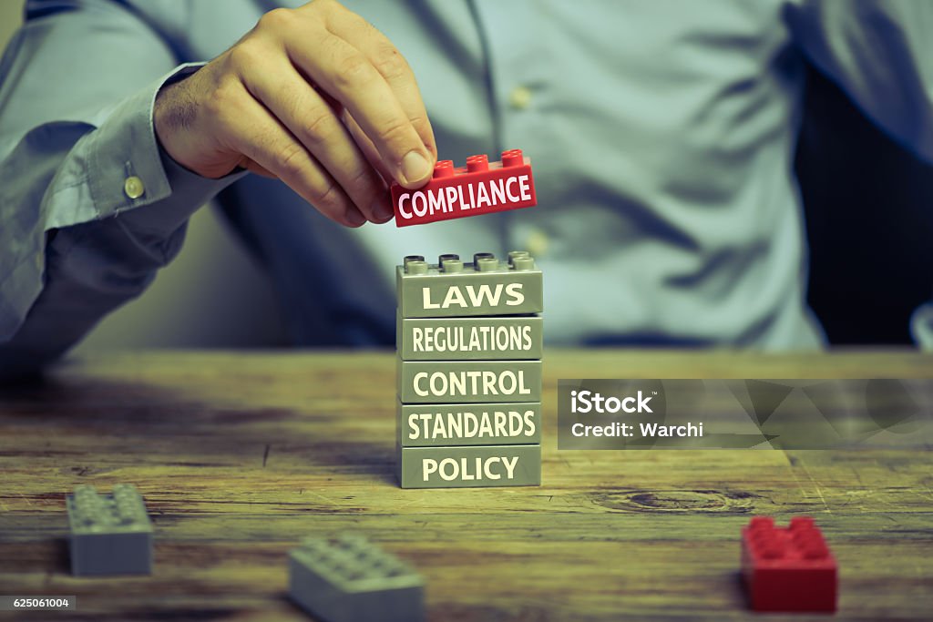 Compliance Man in business shirt playing with toy blocks on wood desk. There are compliance related words printed on the blocks Conformity Stock Photo