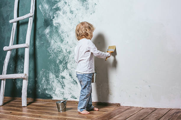 il bambino piccolo bello e felice in jeans dipinge il muro - paintings child house childhood foto e immagini stock