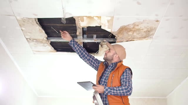 Young man call on the phone in the Service, and public utilities. Ceiling panels damaged huge hole in roof from rainwater leakage.Water damaged ceiling , Insurance case.