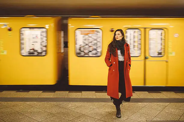 Vintage toned image of a young brunette woman wearing a red coat, standing in the Berlin metro station.