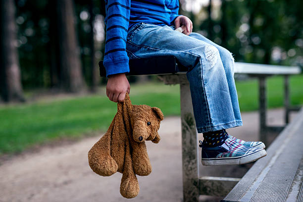 Young boy holding teddybear while alone on the bleachers Young boy holding teddybear while alone on the bleachers hiding place stock pictures, royalty-free photos & images
