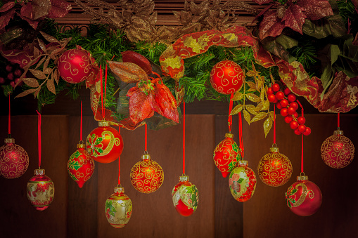 Hanging  red ornate Christmas ornaments with garland  against wooden background. The ornaments have wonderful gold glittered designs on them and the whole look is very old fashioned and Victorian in this horizontal image.