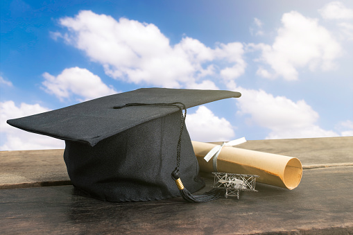 graduation cap, hat with degree paper on wood table, sky background Empty ready for your product display or montage.