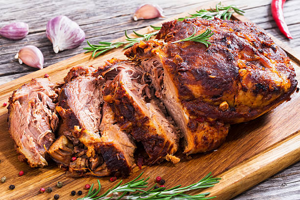 Big Piece of Slow Cooked Oven-Barbecued Pulled Pork shoulder Big Piece of Slow Cooked Oven-Barbecued Pulled Pork shoulder on chopping board with mixed peppercorns, rosemary and garlic, view from above, close-up pork stock pictures, royalty-free photos & images