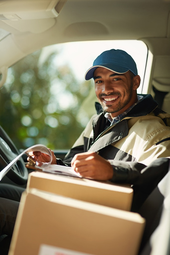 Portrait of a smiling delivery man sitting with boxes in his van