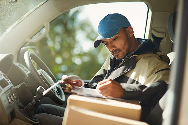Updating his delivery status Shot of a delivery man reading addresses while sitting in a delivery van delivery person stock pictures, royalty-free photos & images