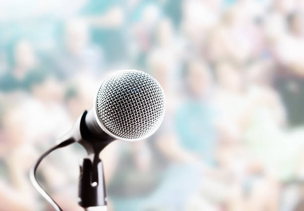 istock Brightly lit microphone in front of defocused audience 625136600