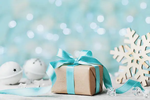 Photo of Christmas gift box, snowflake, jingle bell against blue bokeh background.