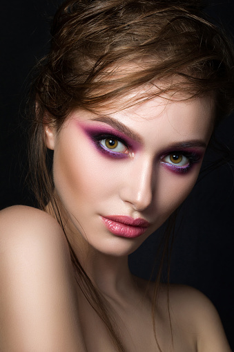 Closeup portrait of young beautiful woman with bright pink smokey eyes and lips over black background. Fashion makeup. Studio shot. Modern spring or summer make up