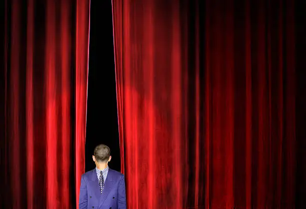 man in reverse side of suit on stage with opening red curtain 