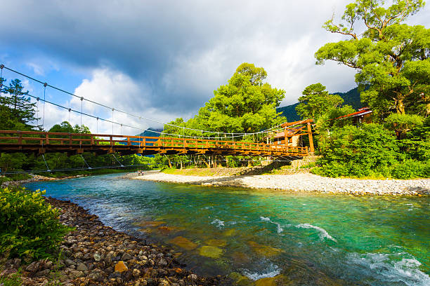 Dramatic stormy morning light shades half of Kappa Bashi Bridge on the riverbanks of Azusa Gawa River in Japanese Alps village of Kamikochi, Nagano, Japan. Horizontal