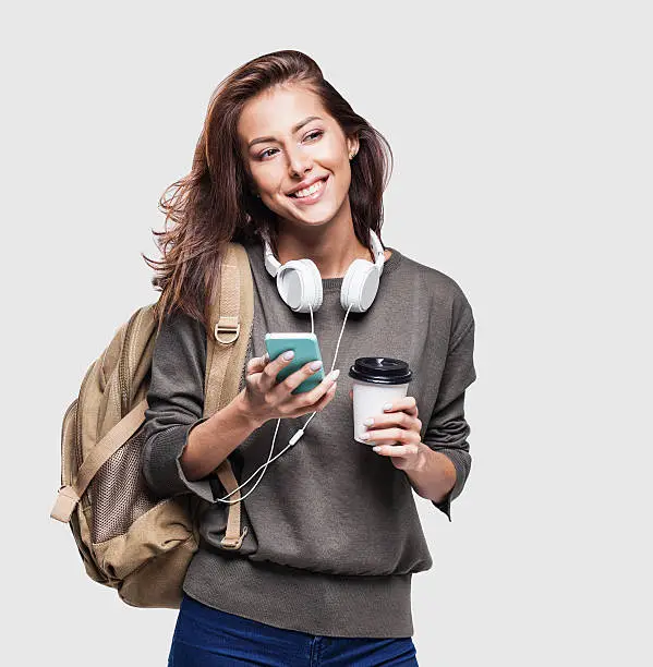 Happy young traveler girl holding smartphone and coffee