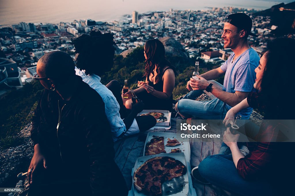 Group of young adult friends having picnic with pizza at Group of young adult friends having picnic with pizza at sunset and watching the city Cape Town Stock Photo