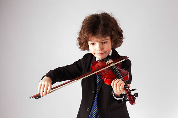 istock Cute curly little boy playing the violin. Gray background. 625192692