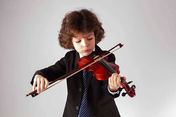 istock Little curly boy playing the violin. Gray background. 625192882