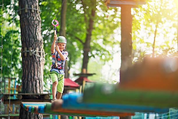 Little boy walking in outdoors ropes course Little boy participating in ropes course in outdoors adventure park. The boy aged 7 is smiling. Sunny summer day. canopy tour photos stock pictures, royalty-free photos & images