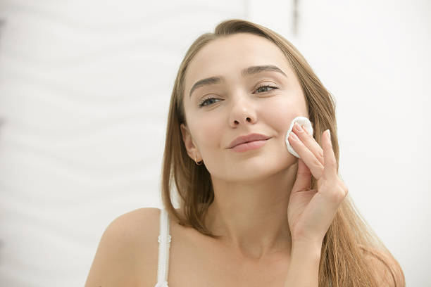 smiling young woman cleaning her skin with a cotton pad, - women beauty innocence make up imagens e fotografias de stock