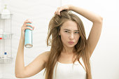 Beautiful young girl applying hair spray on her hair