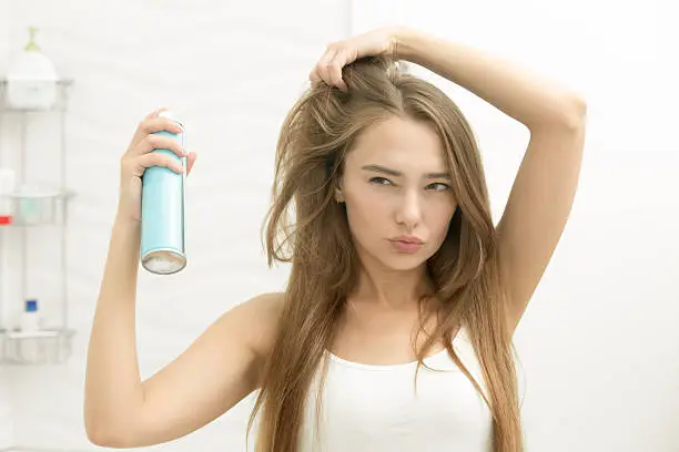 Photo of Beautiful young girl applying hair spray on her hair