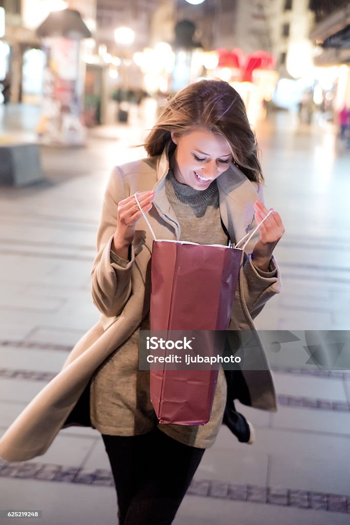 Lovely girl looking at christmas  shopping bag during christmas Happy woman Christmas shopping walking on the street against christmas decoration looking at a gift bag 20-29 Years Stock Photo