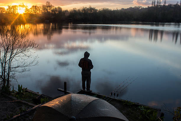 sunrise carp angler overlooking lake - ian 個照片及圖片檔