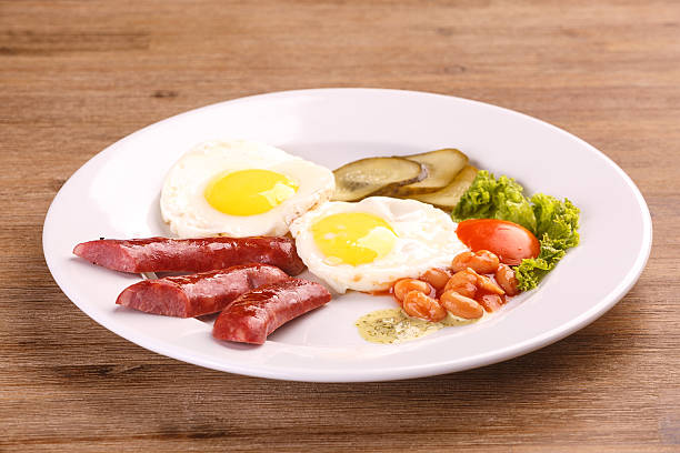 istock Fried eggs with bacon sausages and greens 625235210