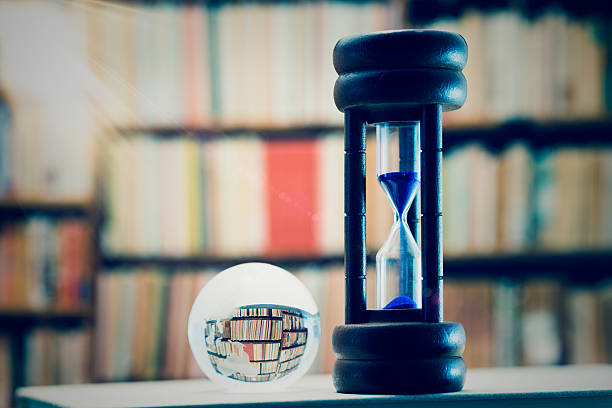 istock Hourglass against book shelf, with lens flare 625235936