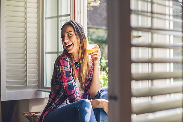 Young woman enjoying fresh orange juice Beautiful woman holding a glass with juice sitting in a country villa, smiling and looking back.  juice drink stock pictures, royalty-free photos & images
