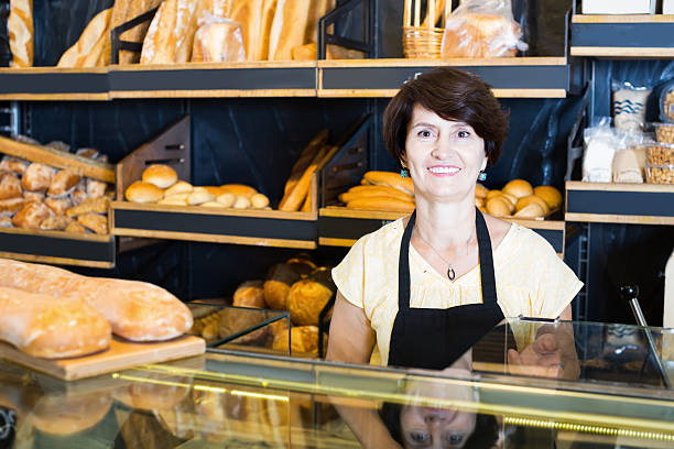 Middle aged woman baker with tasty bread products Middle aged woman baker with tasty bread products on counter old candy store stock pictures, royalty-free photos & images