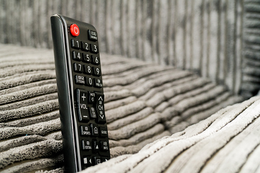 Ever lost your TV remote? This is a picture of a Smart Television Remote stuck in a sofa (couch). Grey couch. Daylight picture of remote control.  Remote is upright in between cushions.