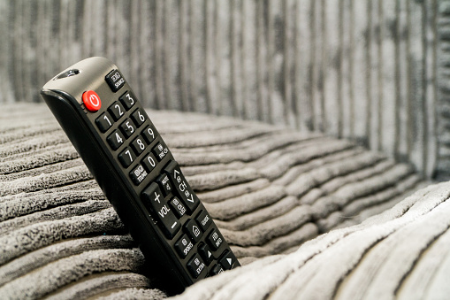 Ever lost your TV remote? This is a picture of a Smart Television Remote stuck in a sofa (couch). Grey couch. Daylight picture of remote control. Remote is standing upright in between cushions.