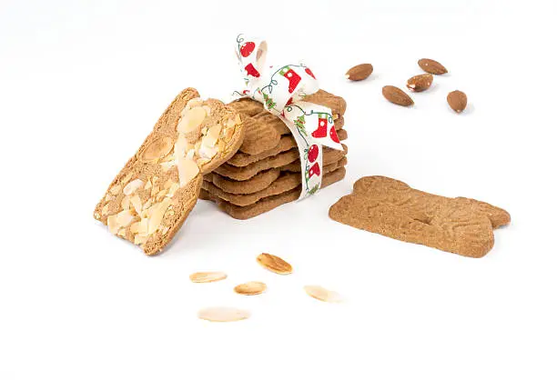 Closeup of a stack of spiced biscuits with almonds ( Spekulatius ) decorated with Christmas Bow, surrounded by almonds and more biscuits on white background.