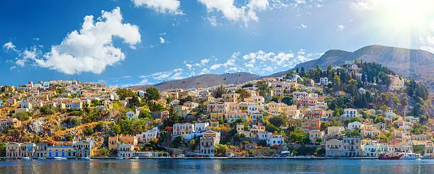 Panoramic shot of the Harbour at Symi Greece with a traditional fishing boat in the foreground. Greece Europe.Symi / Simi Island panorama
