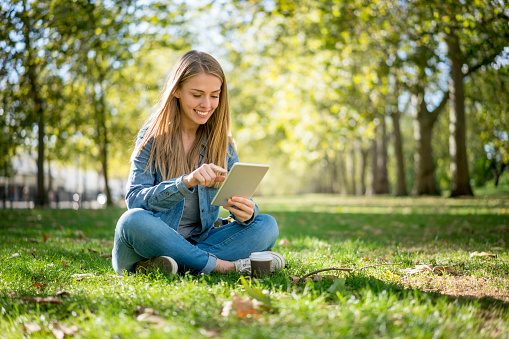 Casual woman relaxing at the park using a tablet computer and looking very happy