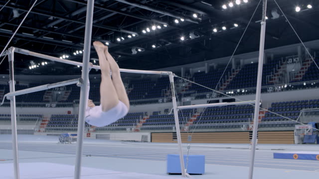 Female gymnast practicing on uneven bars in empty arena