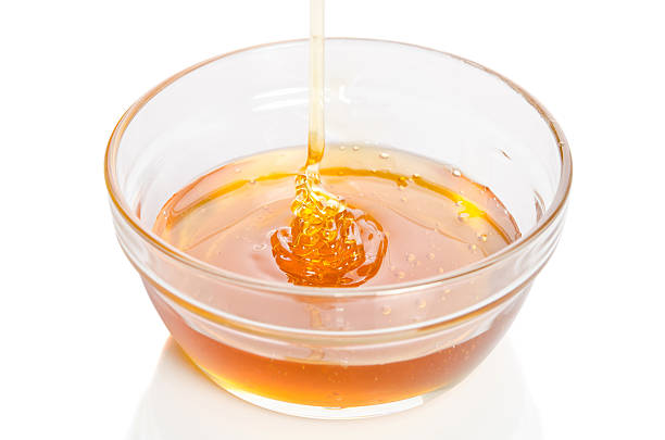 istock Honey dripping into glass bowl isolated on white background 625302546