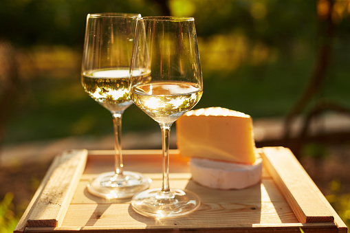 Two glasses of white wine with cheese on wooden box, toned at sunset