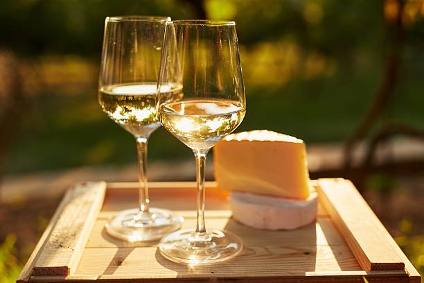 Two glasses of white wine with cheese Two glasses of white wine with cheese on wooden box, toned at sunset chardonnay grape stock pictures, royalty-free photos & images