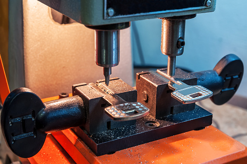 Close-up of a jeweller using rolling mill to flatten a piece of metal while making a ring at a bench in his workshop