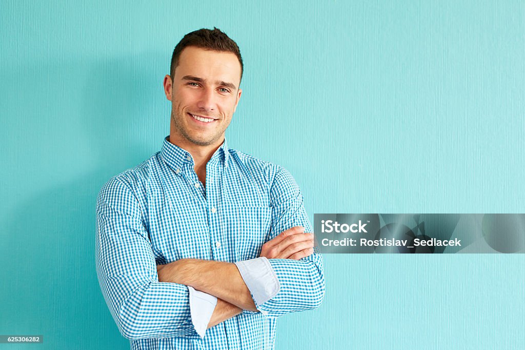Happy man with crossed arms Happy handsome man with crossed arms leaning against a turquoise wall Men Stock Photo