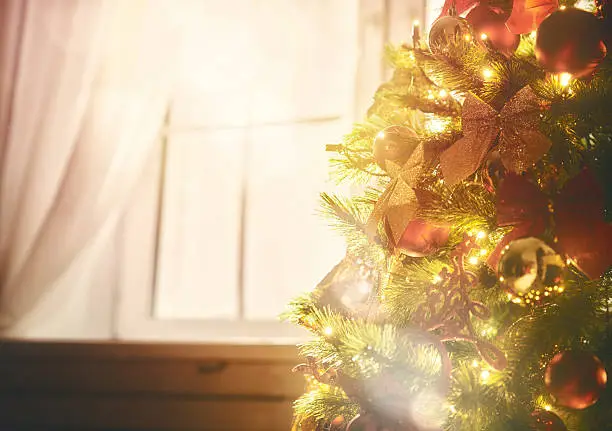 Merry Christmas and happy holidays! Christmas tree with toys baubles close-up on window background.