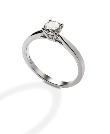 A sparkling solitaire diamond ring is isolated on a white background with a clipping path. The 1-carat diamond is set on a shiny silver platinum band. A ring shaped shadow falls forwards from the ring. The shadow is not included in the clipping path.