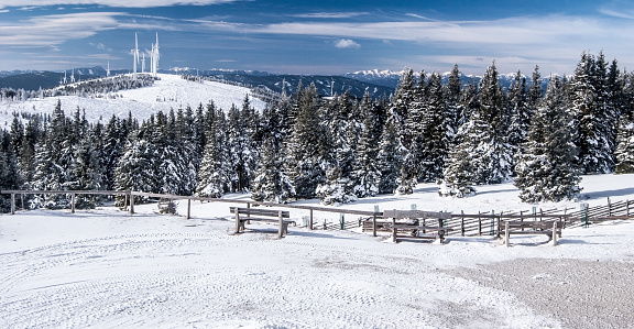 mountain panorama with hills, wind turbine farm, forest and mountain peaks on the background from Roseggerhaus chalet in winter Fischbacher Alpen mountains in Styria