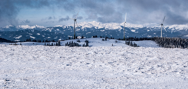 winter austrian alps panorama with hills, wind turbine farm, high mountains with snowy peaks and blue sky with clouds from Grazer Stuhleck hill in Fischbacher Alpen mountains in Styria