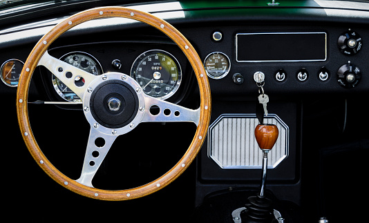 The wooden steering wheel and interior of a classic car.