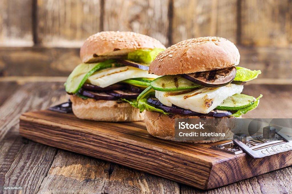 Grilled vegetable and haloumi burger with romaine lettuce Grilled vegetable and haloumi burger with romaine lettuce on wooden table Burger Stock Photo
