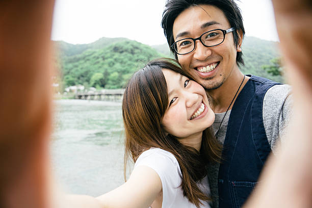 casal japonês alegre tirando selfie ao ar livre em um parque - togetsu kyo bridge - fotografias e filmes do acervo