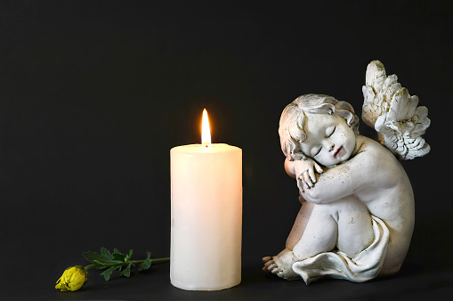 White candle, an angel and flower on dark background