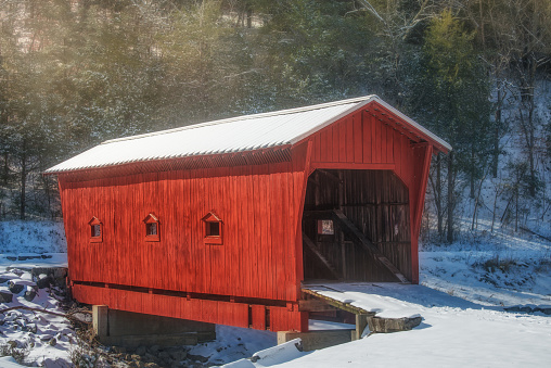 Old, red covered bridge in snow with glowing light.